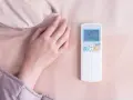 Main tenant ajuste la température clim pour dormir. La télécommande affiche 25 degrés.