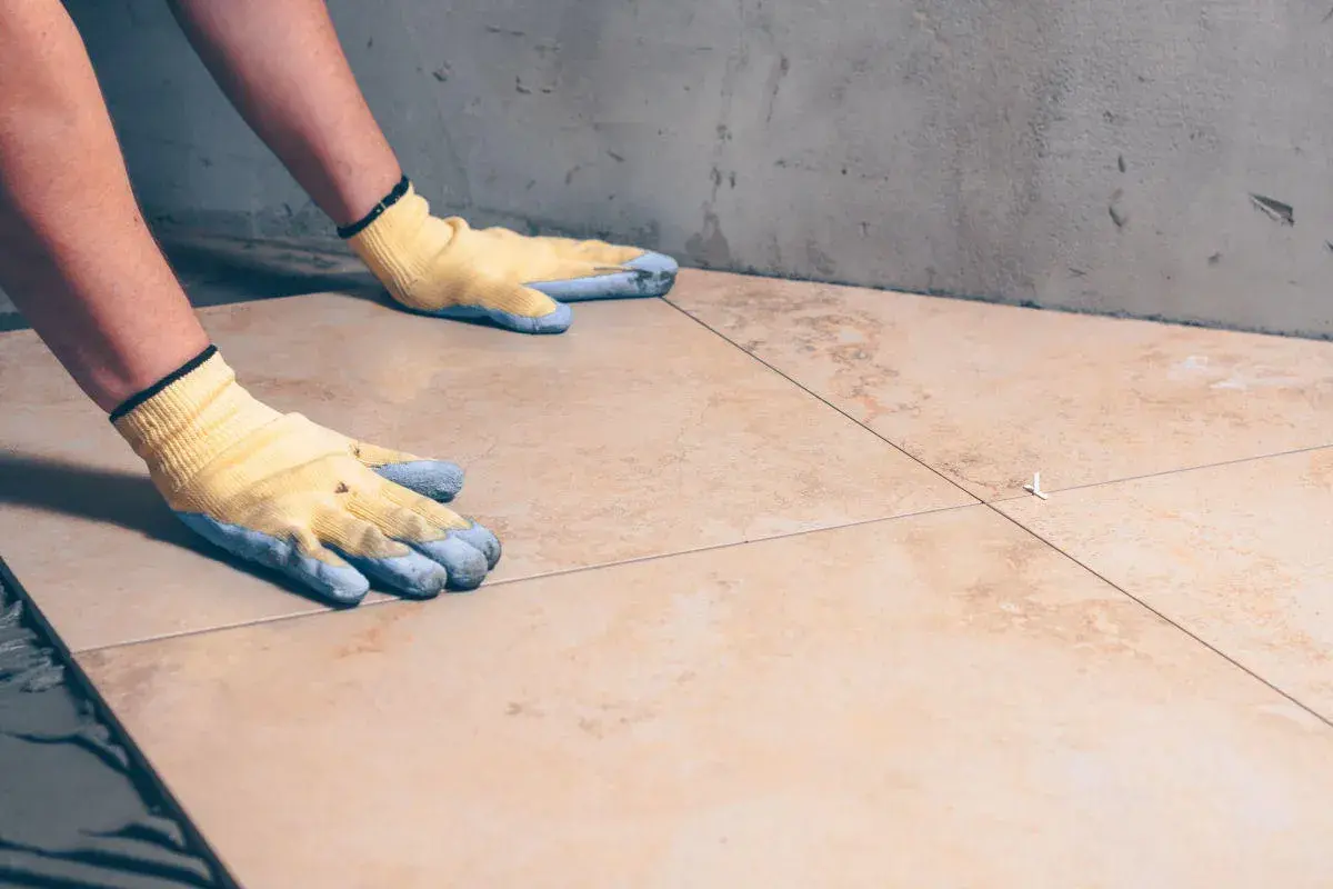 Pose de carrelage avec des gants, assurant l'étanchéité sur carrelage existant.
