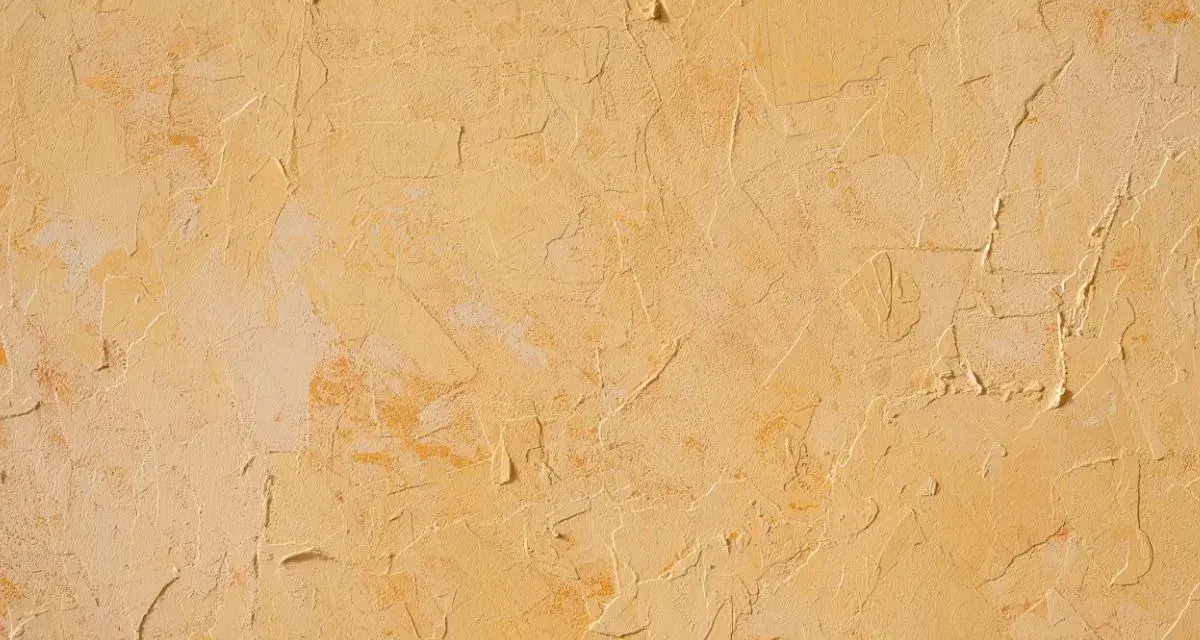 Texture d'un enduit taloché ou gratté, aux nuances chaudes de jaune et d'ocre, évoquant un mur ancien patiné par le temps.