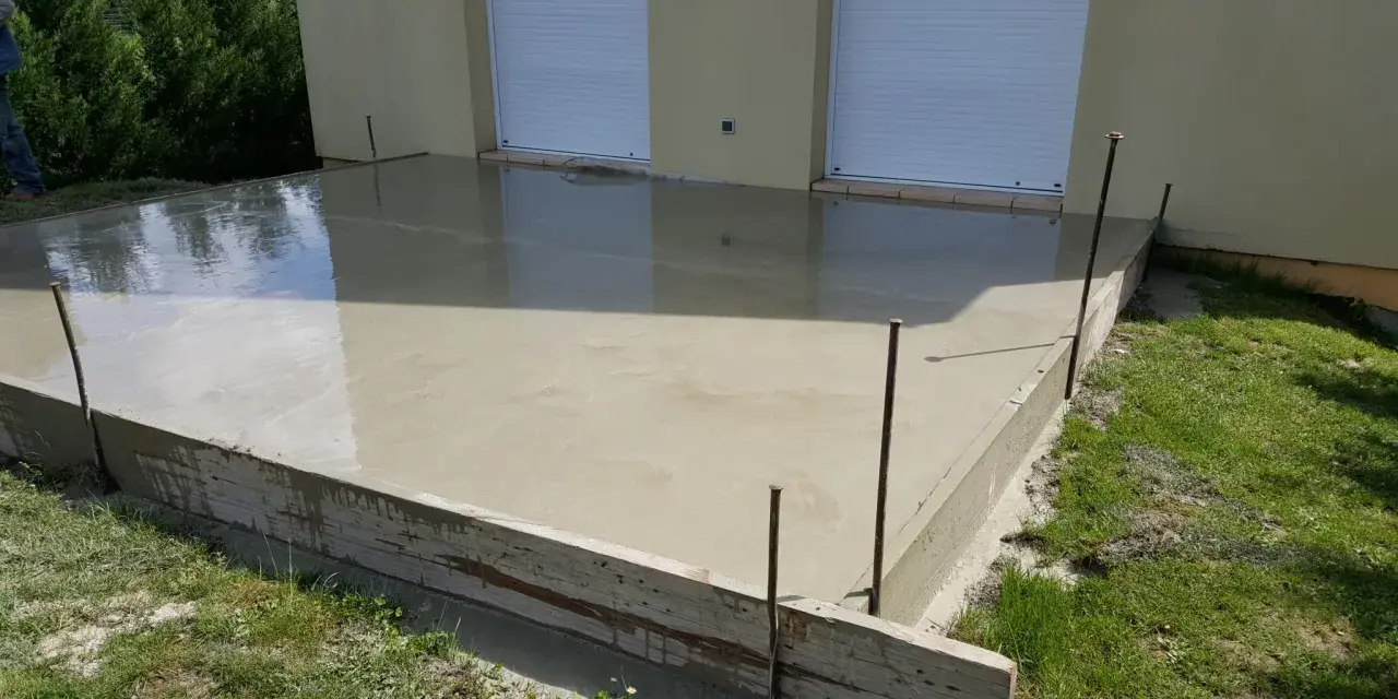 Dalle en béton fraîchement coulée pour une maison, avec coffrage en bois et ferraillage apparent. L'épaisseur de la dalle est visible.