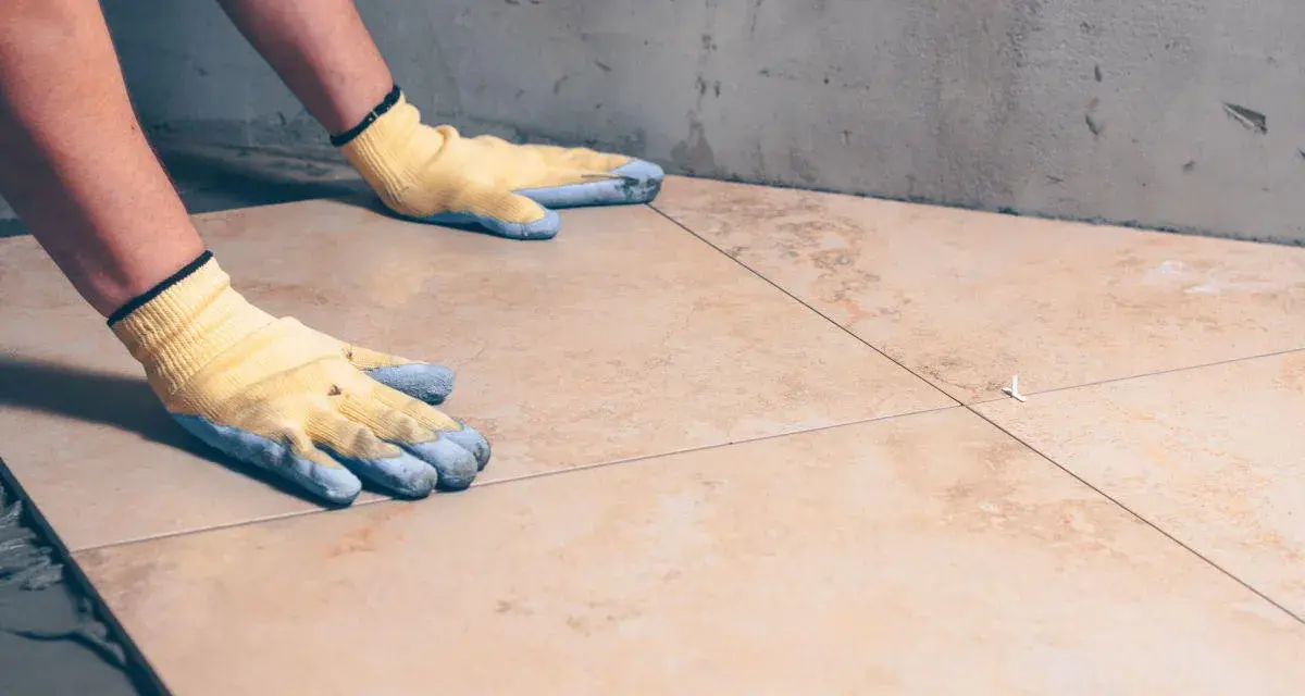 Pose de carrelage avec des gants, assurant l'étanchéité sur carrelage existant.