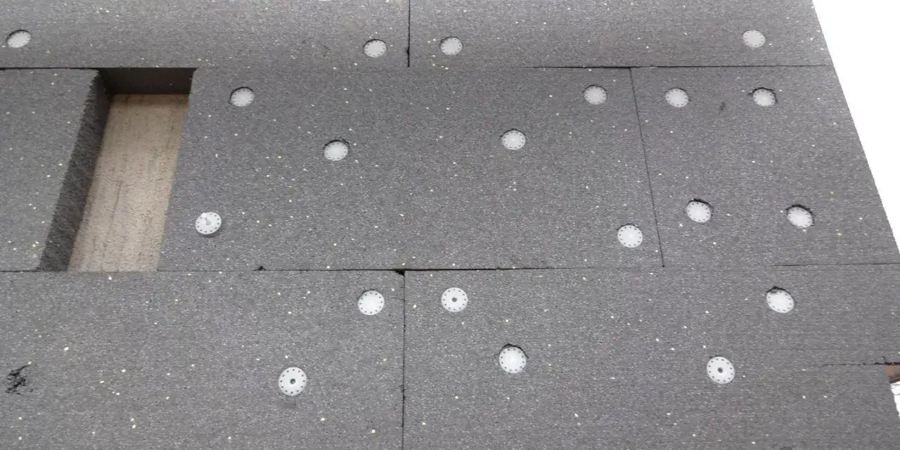 Panneau de polystyrène gris avec des fixations blanches. On compte 3 à 4 chevilles par plaque de polystyrène pour l'isolation.