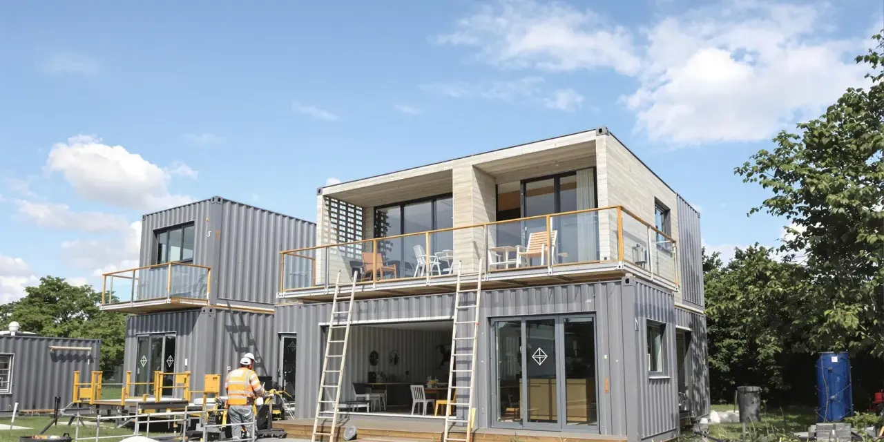 Maison en container prix : construction moderne à deux étages avec balcons, fenêtres panoramiques et un ouvrier en gilet de sécurité.