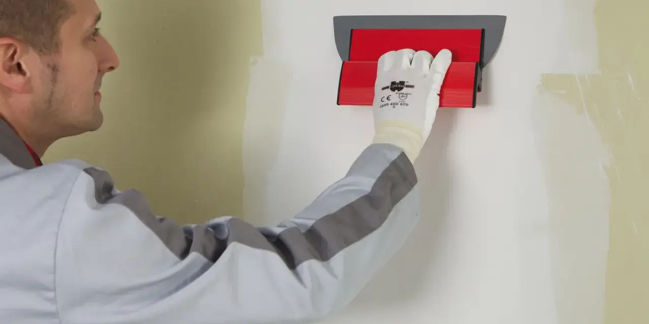 Un ouvrier utilise un outil pour appliquer une bande de placo sur un mur.