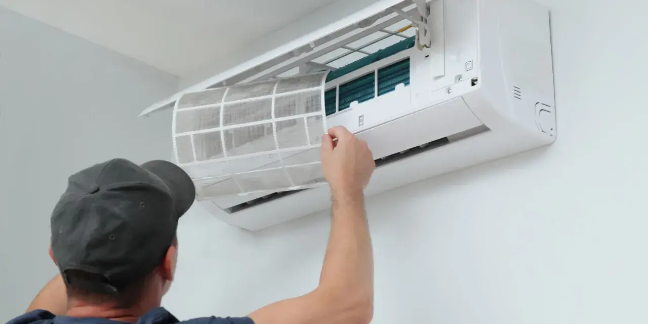Un homme retire un filtre à air sale d'une unité de climatisation murale, étape essentielle de l'entretien climatisation maison pour un air sain.