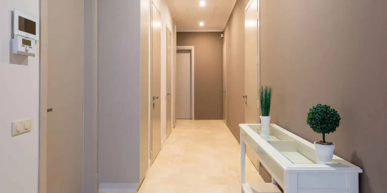Peinture couloir et portes aux tons neutres, sol en marbre clair, console blanche avec plantes décoratives.