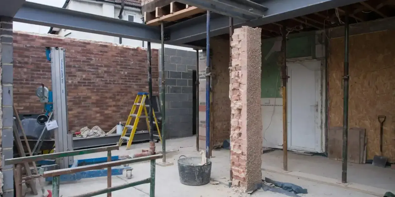 Travaux de rénovation : agrandir ouverture mur porteur avec poutres métalliques. Échafaudages, briques et outils sur le chantier.