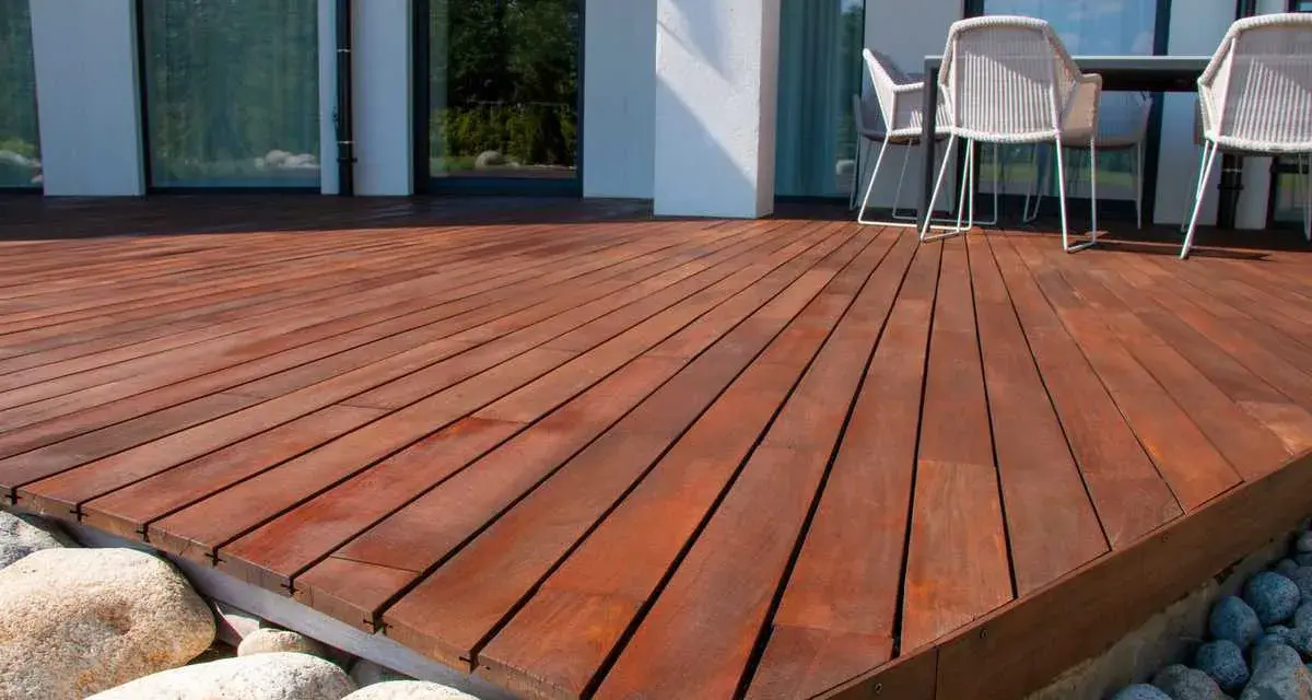 Belle terrasse en bois sur plot, avec des meubles de jardin et des rochers.