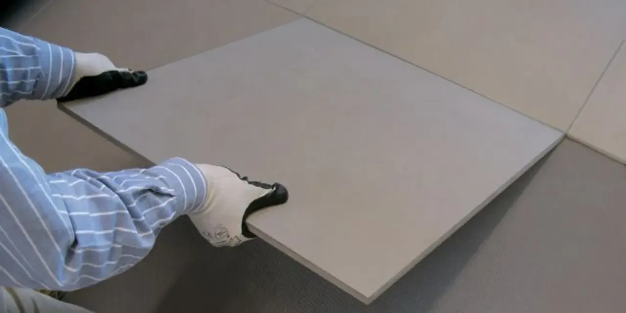 Pose d'une nouvelle dalle pour coller du carrelage sur du carrelage. Les mains gantées ajustent la pièce sur le sol existant.