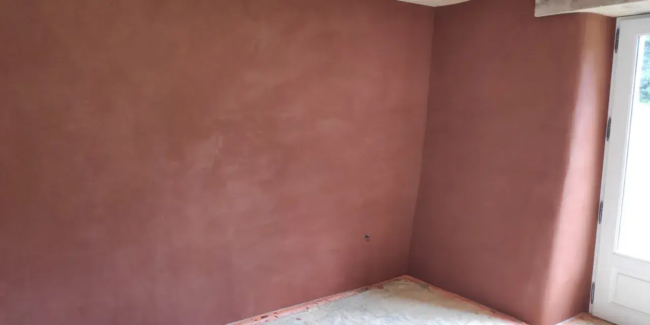 Un coin de pièce aux murs recouverts d'un enduit chaux sable ocre. Le sol est protégé par une bâche. Le plafond est en bois clair.