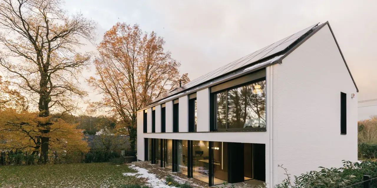 Agrandissement maison ossature bois moderne avec panneaux solaires, entourée d'arbres aux couleurs d'automne et d'un jardin enneigé.