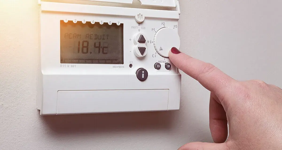 Main d'une femme ajustant un cee thermostat connecté affichant 18.4°C.