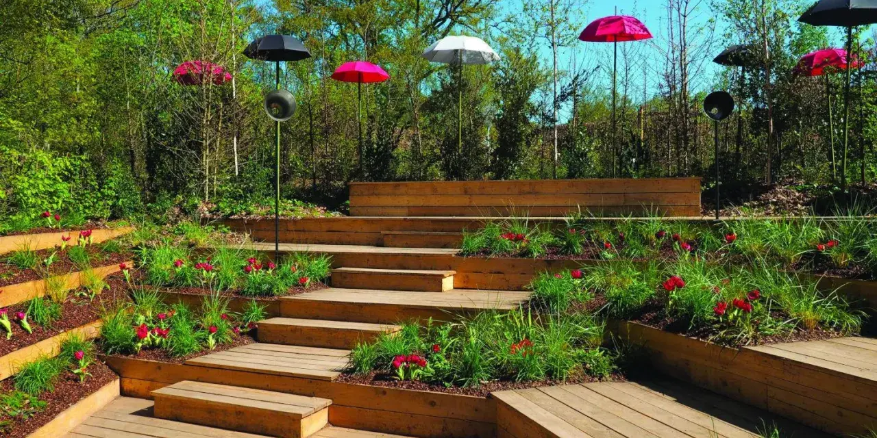 Un jardin aménagé avec des terrasses en bois et une **profondeur marche escalier extérieur** sur plusieurs niveaux, décoré de tulipes rouges et de parasols colorés.