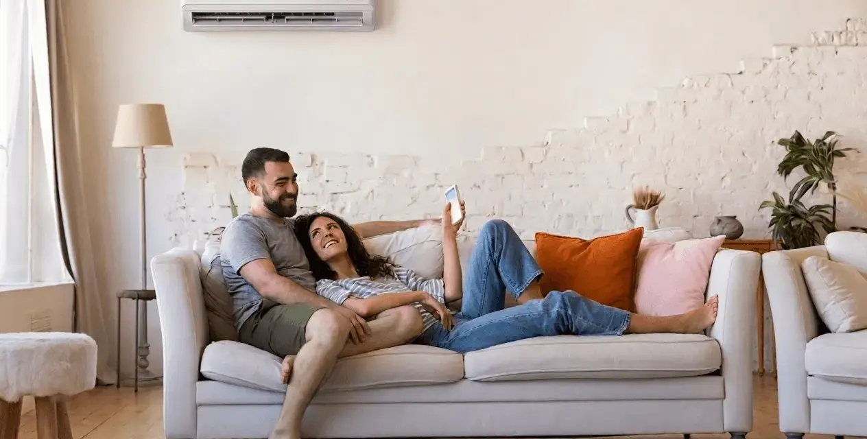 Couple détendu sur un canapé, profitant du confort d'une climatisation réversible. Aide EDF pour un intérieur agréable.