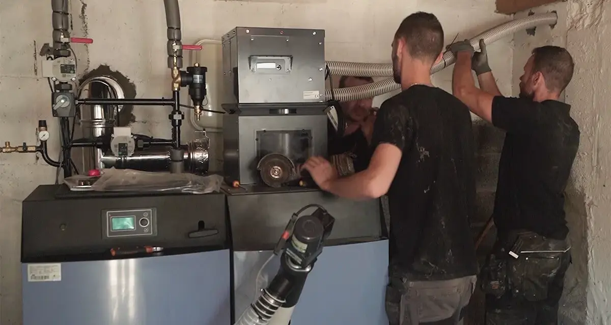 Techniciens installant une nouvelle chaudière, remplaçant une ancienne chaudière fioul. Travaux de chauffage en cours.