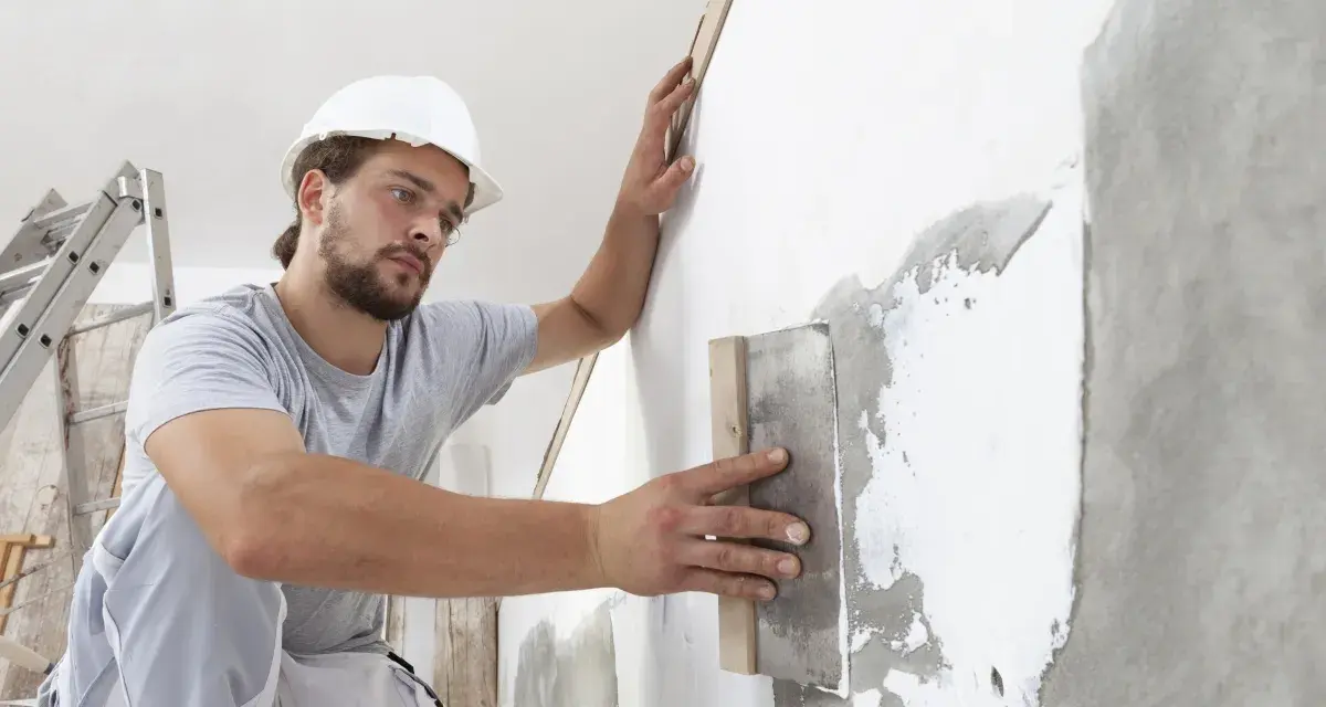 Artisan appliquant un enduit sur béton intérieur, préparant le mur pour une finition parfaite.