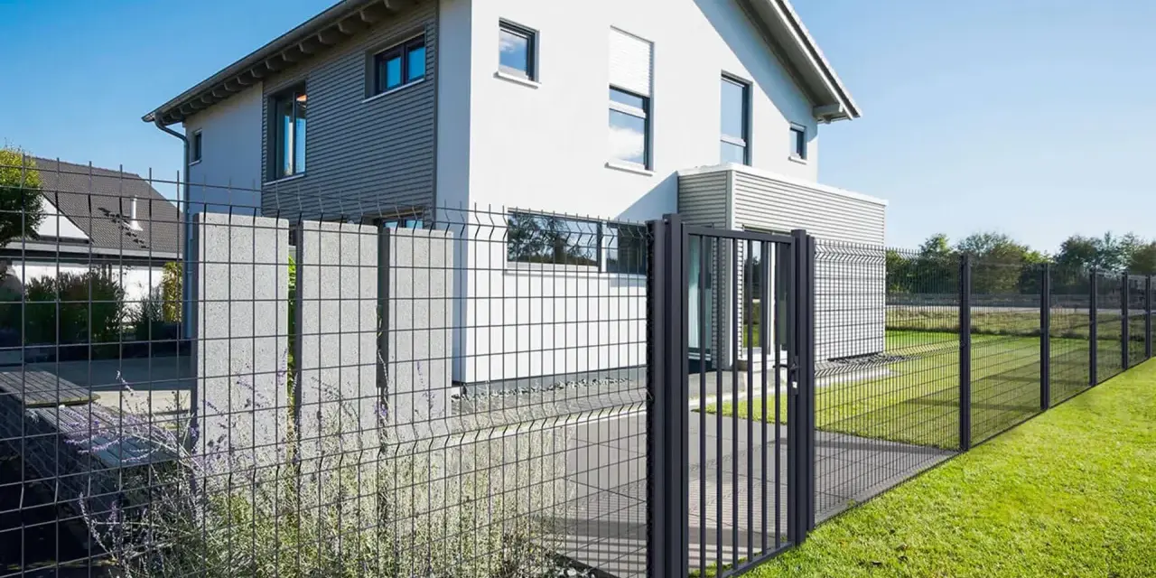 Une clôture privative en limite de propriété délimite un jardin moderne avec une maison blanche et un portillon.