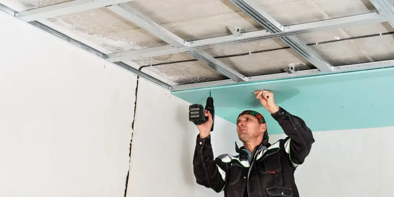 Un ouvrier réalise le schema montage placo plafond, fixant une plaque verte sur une structure métallique.