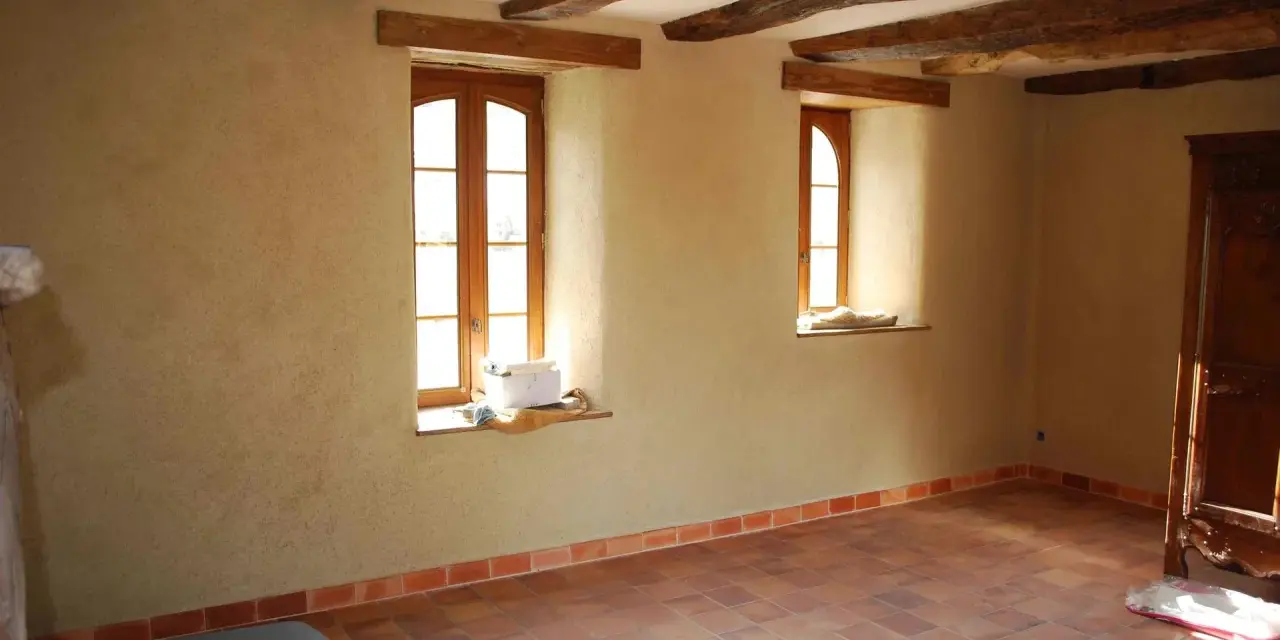 Intérieur d'une pièce aux poutres apparentes, murs en chaux chanvre pour une isolation naturelle, sol carrelé.