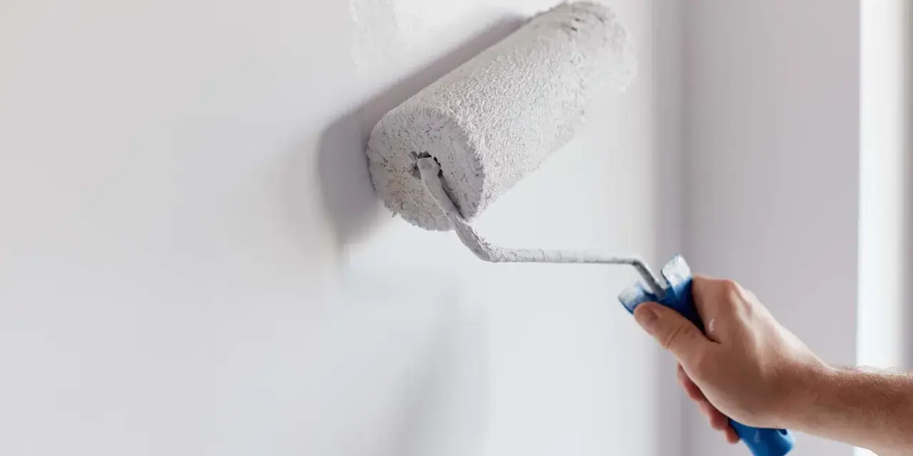 Main d'homme appliquant de la peinture blanche sur un mur avec un rouleau. Un guide visuel pour comment peindre un mur.