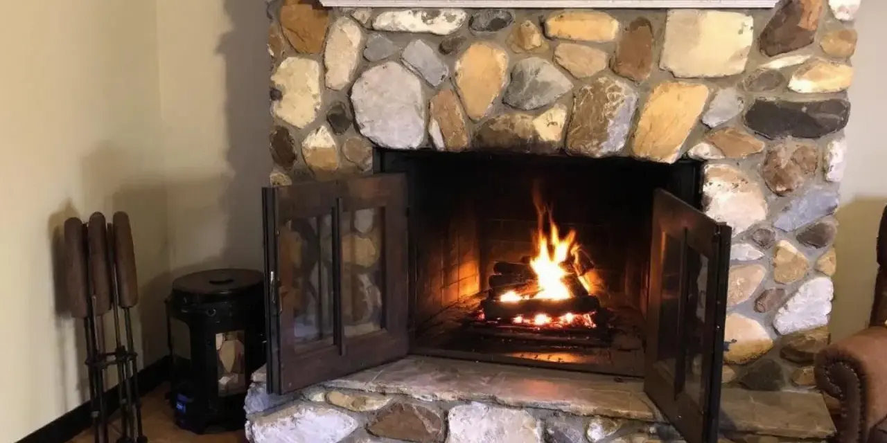 Un feu crépite dans une cheminée en pierres. Quel parement derrière poêle à bois, avec des accessoires de cheminée à gauche.