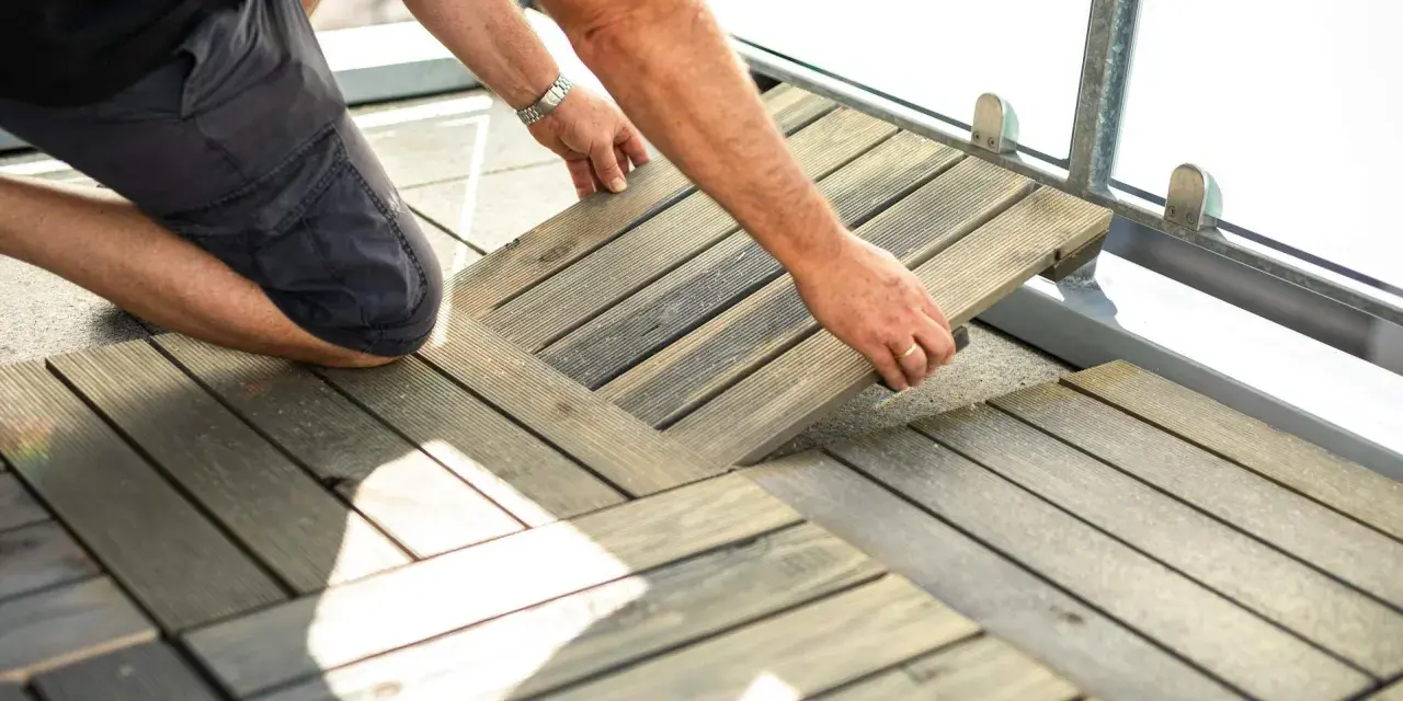 Un homme installe des dalles de terrasse en bois sur son balcon. Une belle idée sol balcon pour un espace extérieur accueillant.