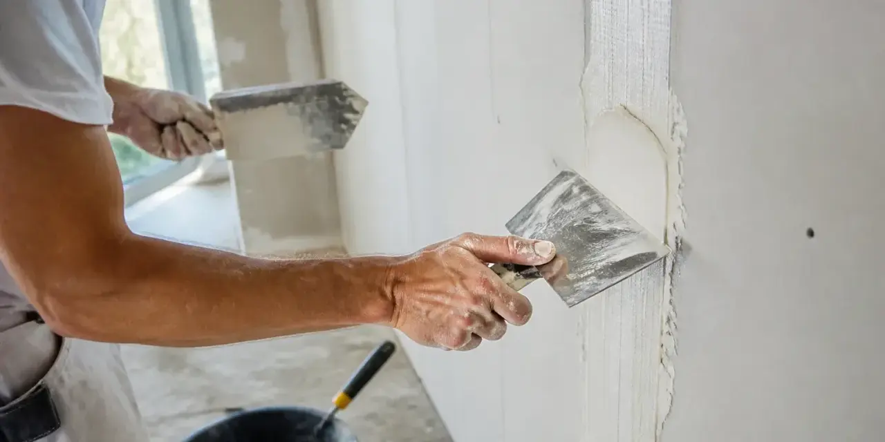 Un ouvrier applique de l'enduit sur une bande de placo. La question "faut-il humidifier les bandes placo" est au cœur de ce travail de finition.