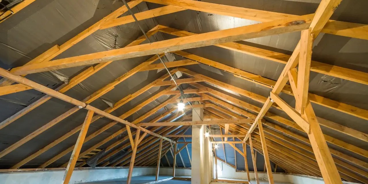 Charpente de grenier en bois, avec une bâche noire recouvrant le toit, suggérant une isolation rampant par l'intérieur en cours.