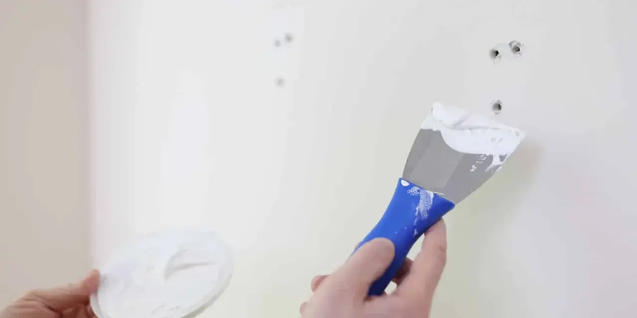 Main tenant en main une spatule chargée de mastic, prêt à reboucher trou mur.