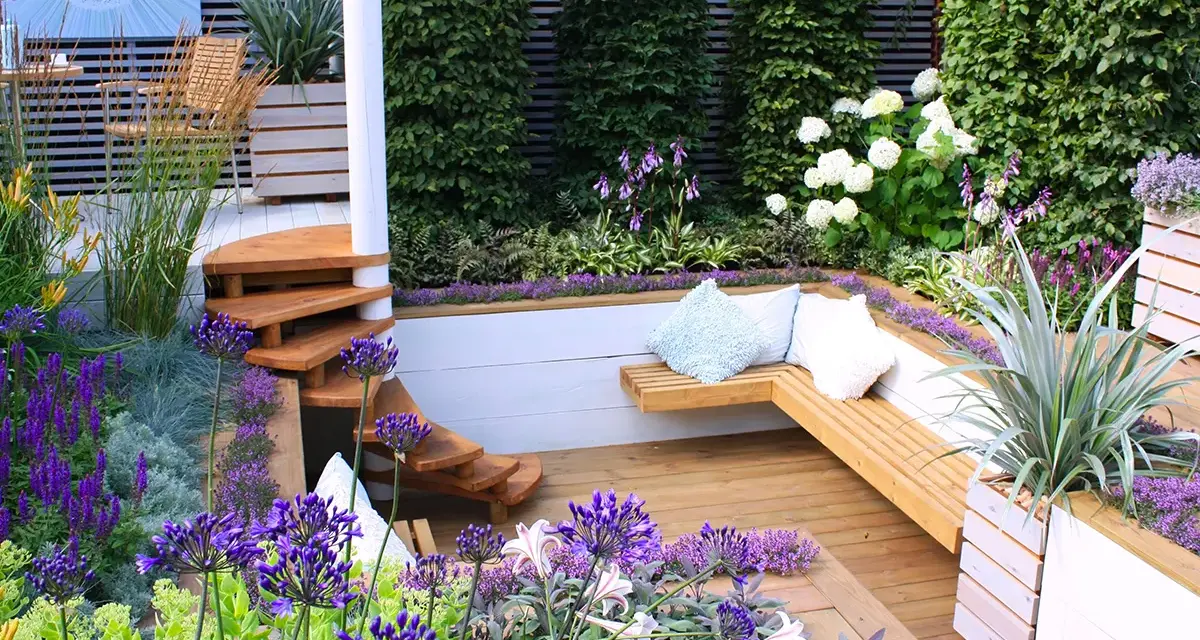 Magnifique terrasse en bois avec banquette intégrée, escalier en colimaçon et fleurs violettes. Idéal pour fabriquer banquette bois terrasse.