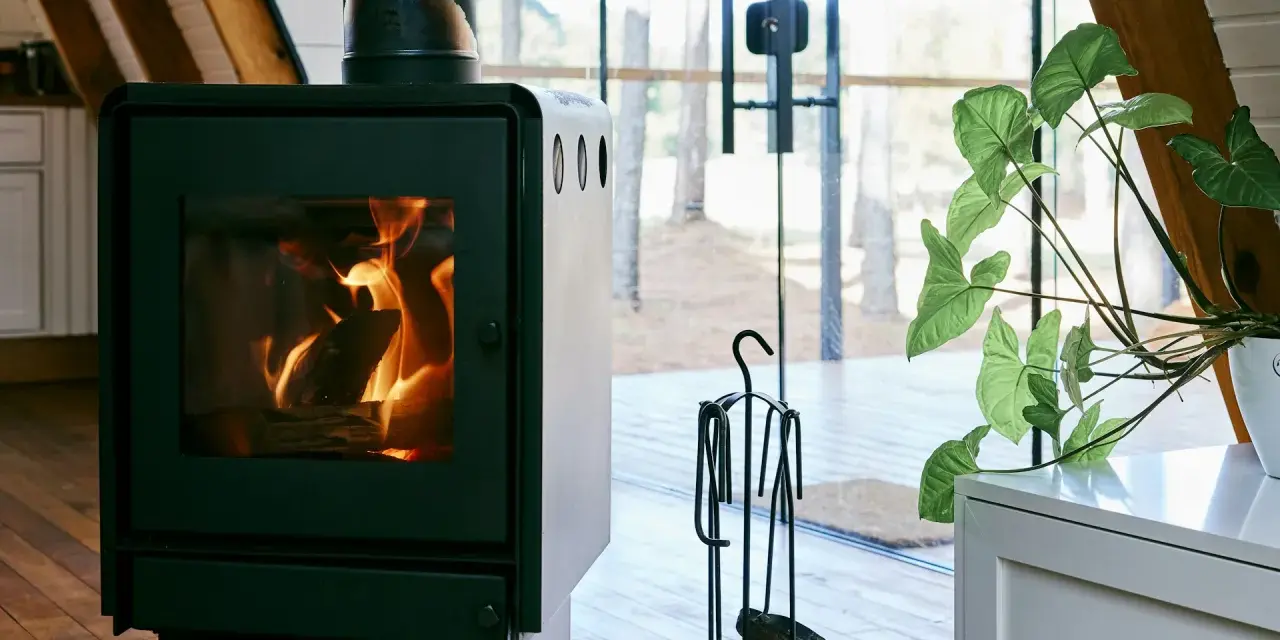 Un poêle à bois MCZ crépitant dans un chalet moderne, avec une grande baie vitrée donnant sur la forêt. Un avis positif s'impose pour ce coin cosy.