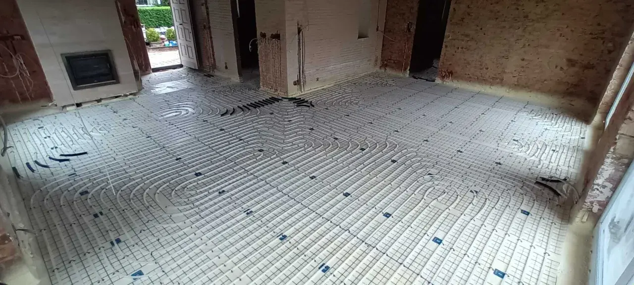Installation d'un plancher chauffant en cours de renovation. Les tuyaux blancs sont posés sur des panneaux isolants, prêts à être recouverts.