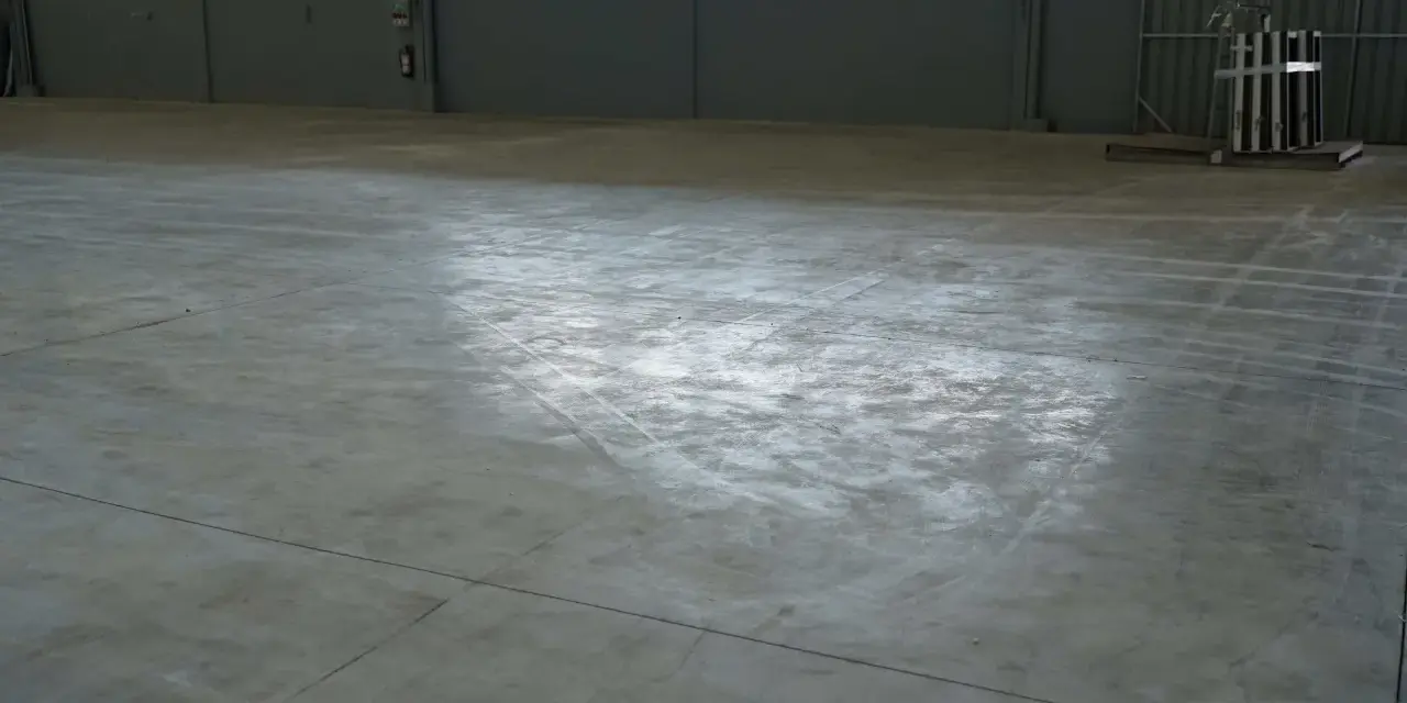 Vaste entrepôt avec une dalle béton qui part en poussière, marquée par des traces de passage.