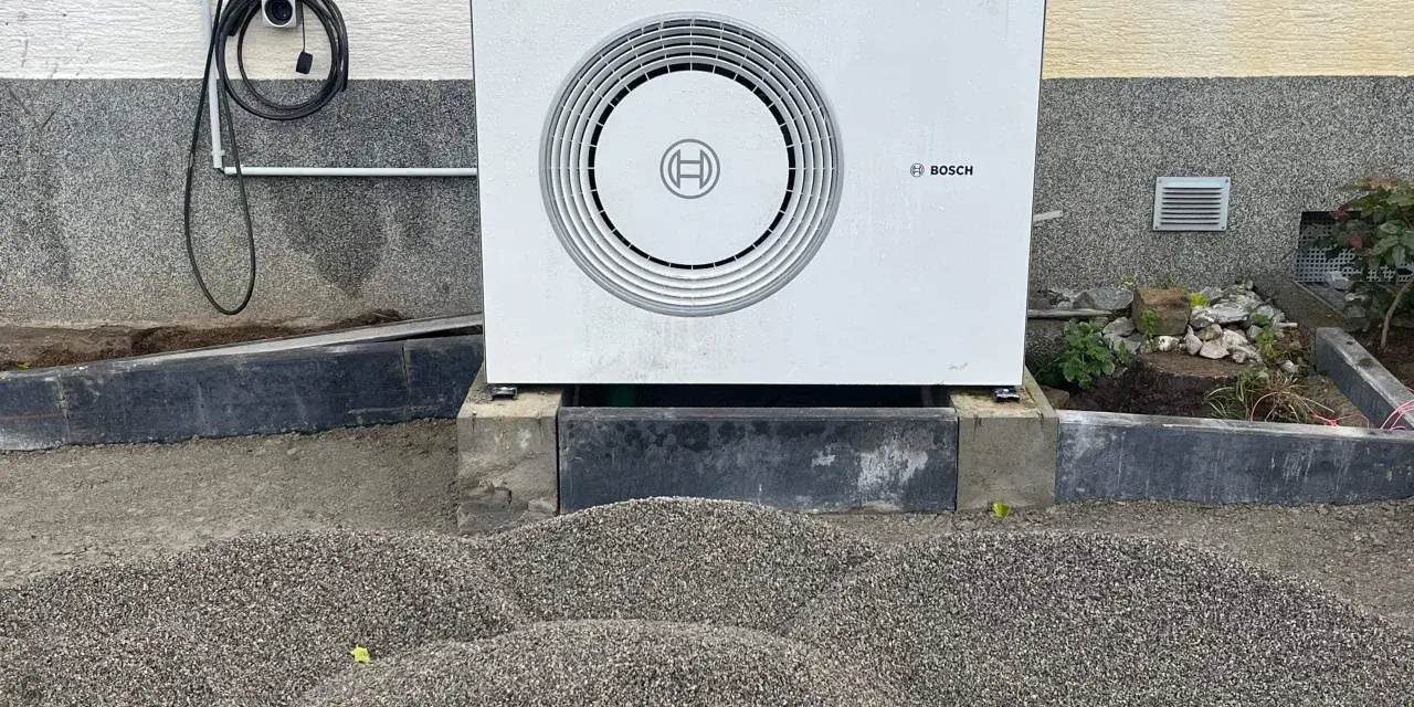 Unité extérieure d'une chaudière à condensation Bosch, installée sur des blocs de béton, avec un chargeur mural à proximité.