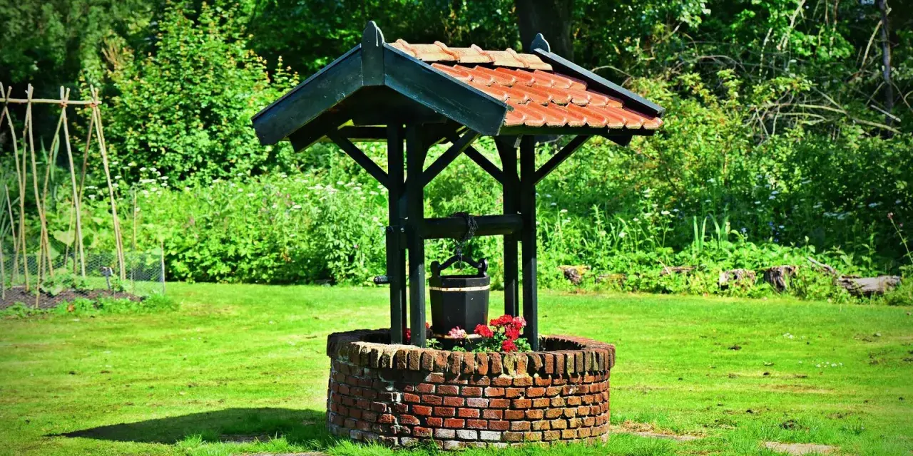 Un puits de briques rouges, orné de fleurs, avec un seau suspendu, prêt à creuser un puits pour abreuver le jardin verdoyant.