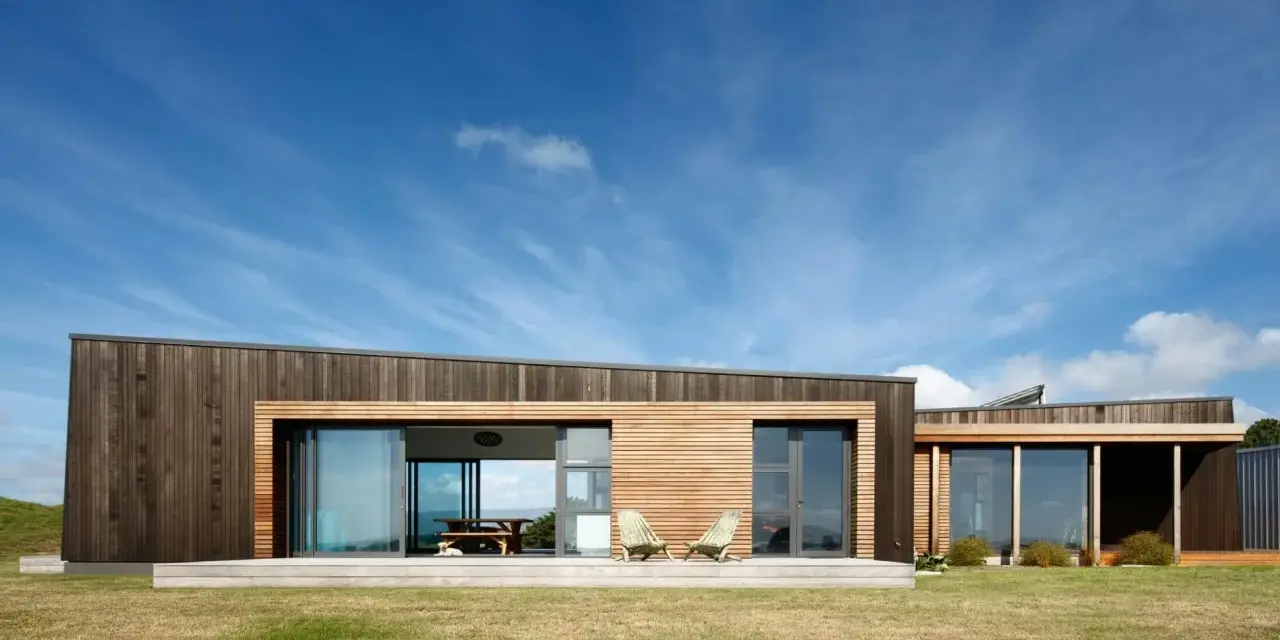 Maison moderne en bois avec grande baie vitrée, deux chaises invitantes sur la terrasse. Une extension maison container stylée.