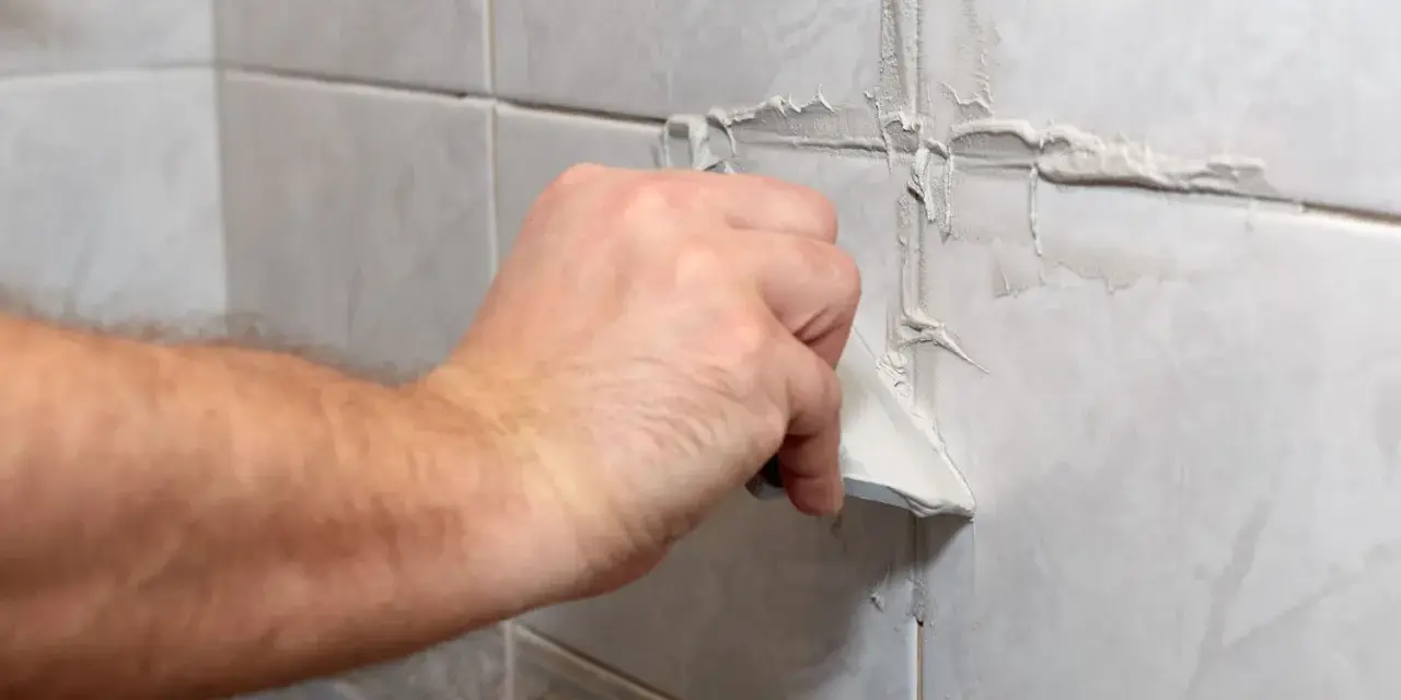 Main tenant enlève du joint de carrelage sec avec une spatule.