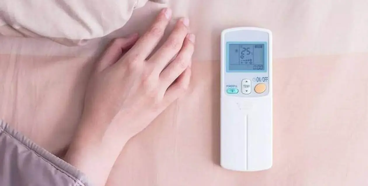 Main tenant ajuste la température clim pour dormir. La télécommande affiche 25 degrés.