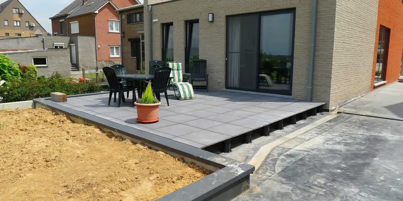 Une terrasse moderne en cours de création, avec des dalles grises surélevées par des plots. Un espace extérieur prêt à être aménagé.