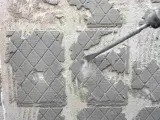 Outil de burinage en action pour enlever colle carrelage sur un mur en béton.