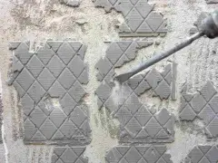 Outil de burinage en action pour enlever colle carrelage sur un mur en béton.