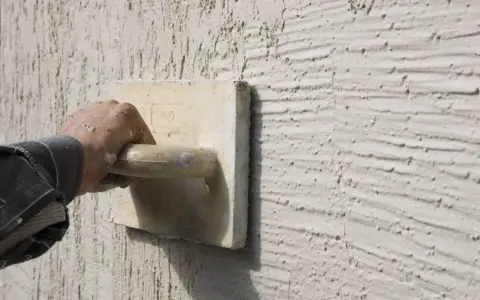Main d'un artisan appliquant un enduit projeté texturé. Le prix au m2 de ce type de finition est souvent demandé.