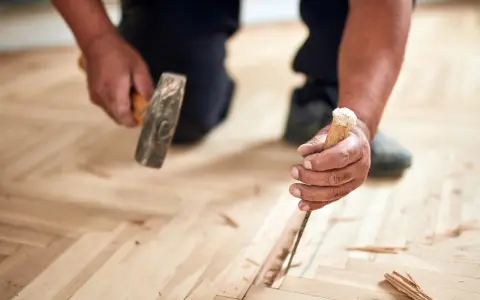 Un artisan utilise un ciseau et un marteau pour changer une lame de parquet flottant endommagée.