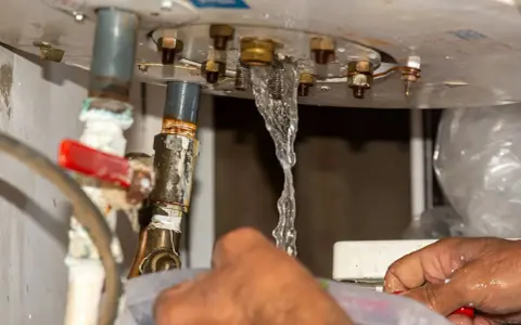 Fuite d'eau par le haut du chauffe-eau, près d'un joint rouge. Un filet d'eau s'échappe des raccords métalliques.