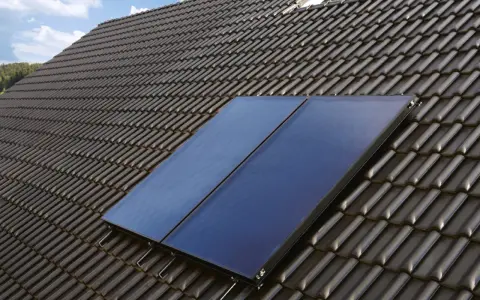 Deux panneaux de chauffage solaire thermique installés sur un toit en tuiles sombres, sous un ciel bleu.