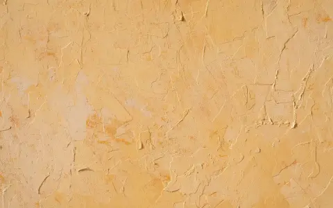Texture d'un enduit taloché ou gratté, aux nuances chaudes de jaune et d'ocre, évoquant un mur ancien patiné par le temps.