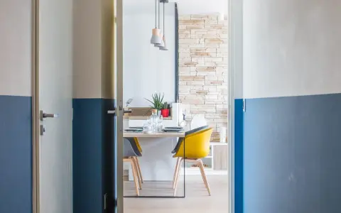 Peinture bicolore sur les murs d'un couloir et de portes, ouvrant sur une salle à manger moderne avec des chaises colorées.