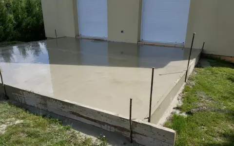 Dalle en béton fraîchement coulée pour une maison, avec coffrage en bois et ferraillage apparent. L'épaisseur de la dalle est visible.