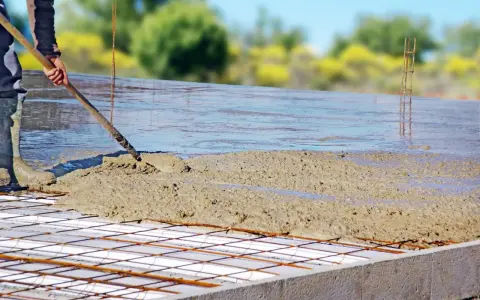 Coulée de béton frais sur une armature métallique pour assurer l'épaisseur dalle maison. Le travailleur étale le béton avec une pelle.