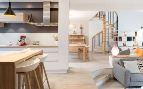 Cuisine moderne avec îlot, escalier hélicoïdal et salon. Cette maison, aux caractéristiques des années 70, allie confort et design.